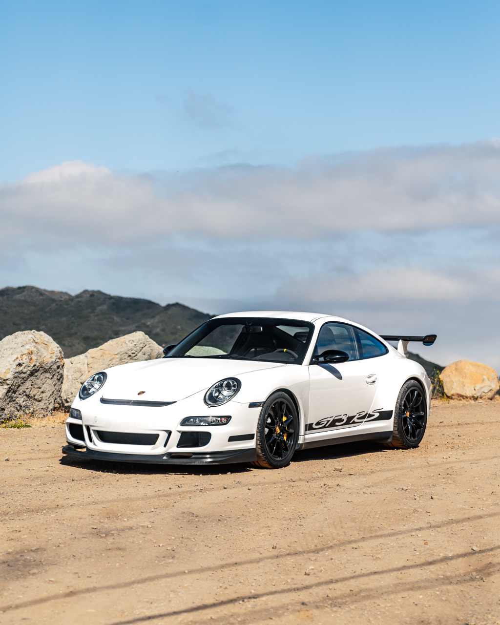 Porsche 911 GT3 RS (997.2), white with black GT3 RS livery, parked on a dirt overlook